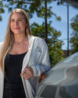 lifestyle image showing a woman smiling while wearing a VP Racing Ogio Ladies Ivory Cardigan and leaning against a car