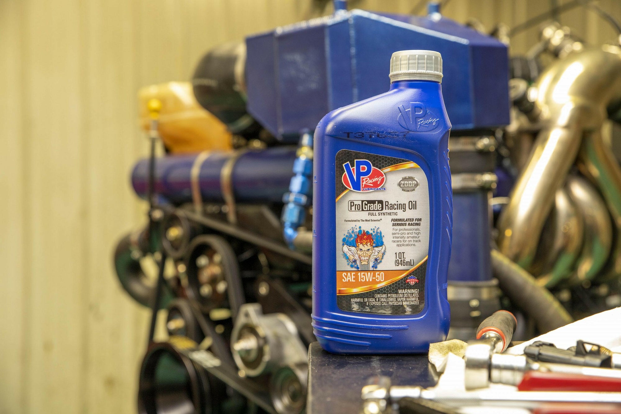 lifestyle image showing a bottle of Pro Grade 15W50 synthetic oil sitting on counter with a racing engine in the background