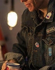 lifestyle image of a male wearing a denim jacket that features the Mad Scientist Bobblehead Enamel Pin and other VP Racing pins