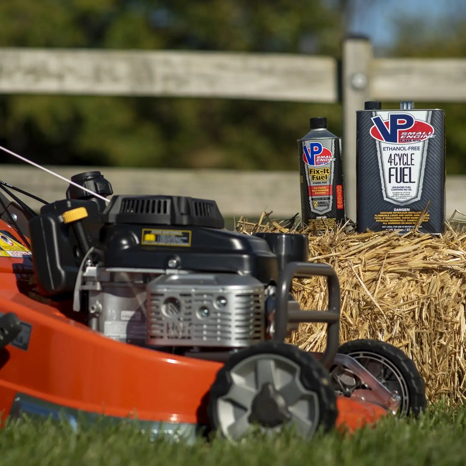 Lifestyle image showing the front of a lawn mower in the foreground and a one-gallon can of VP 4-cycle fuel in the background sitting atop a short bale of hay.