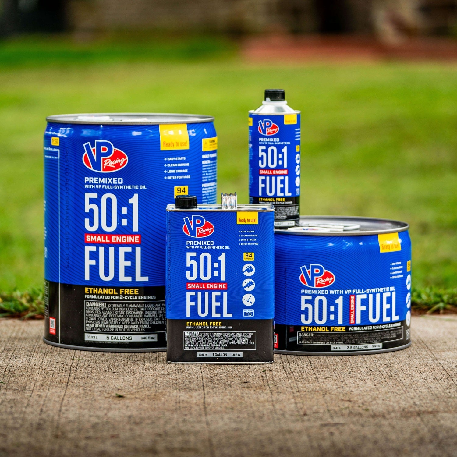 Family shot of VP Racing 50:1 fuel containers, from quart-size to a 5-gallon pail, displayed on concrete with grass in the background.