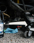 lifestyle image of a bottle of VP Hi-Performance 80w90 GL5 gear oil sitting on the ground beneath a car that has been raised on a jack