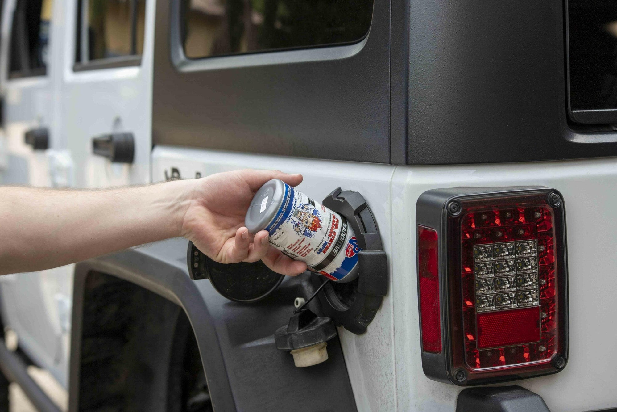 lifestyle image showing a closeup of someone pouring a bottle of VP fuel system cleaner into a gas tank of a Jeep