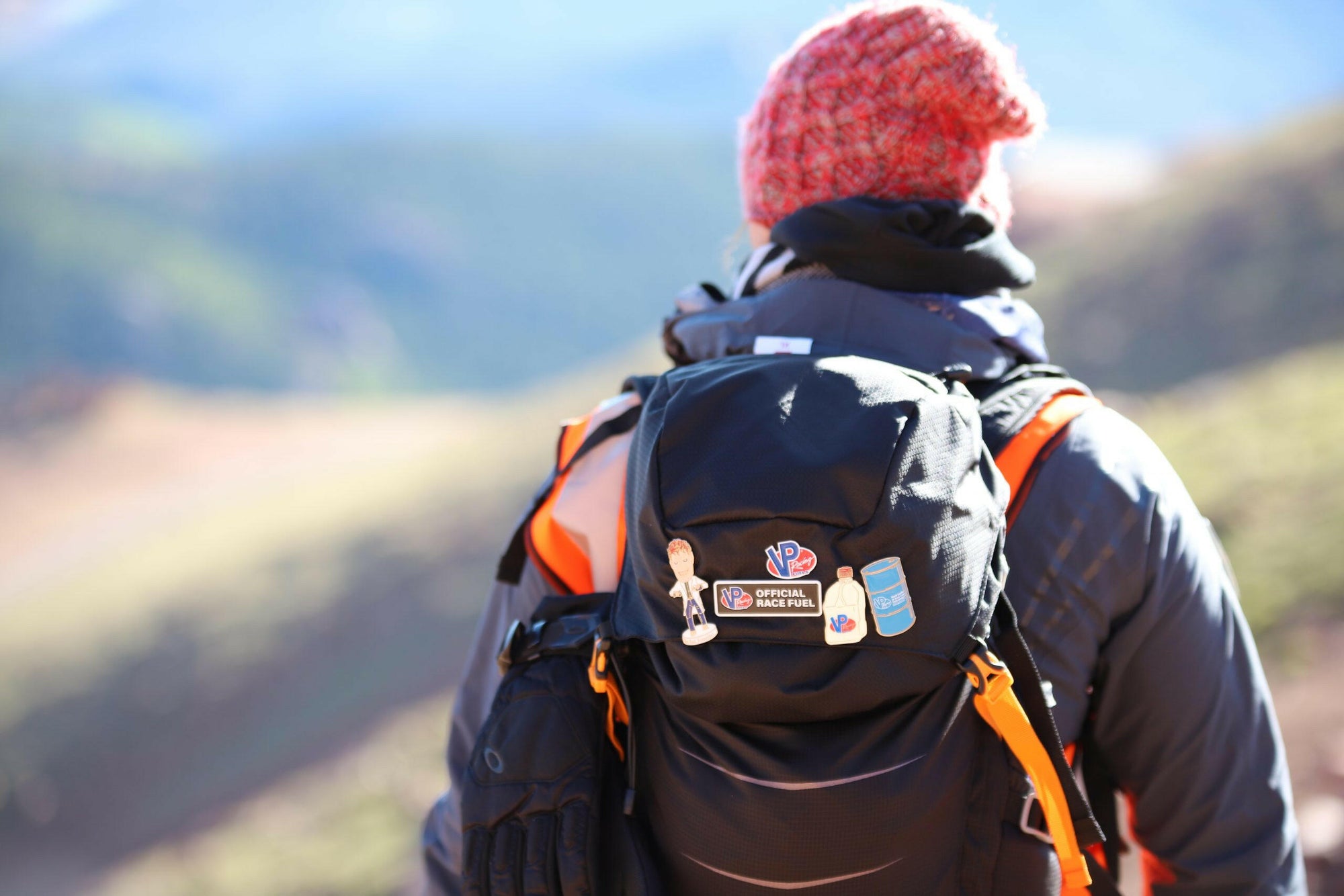 lifestyle image of a hiker wearing a backpack that features the Mad Scientist Bobblehead Enamel Pin and other VP Racing pins