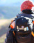 lifestyle image of a hiker wearing a backpack that features the Mad Scientist Bobblehead Enamel Pin and other VP Racing pins