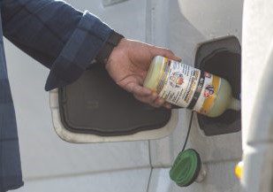 bottle of VP All-In-One Diesel injector cleaner and fuel conditioner being poured into fuel tank of pickup truck