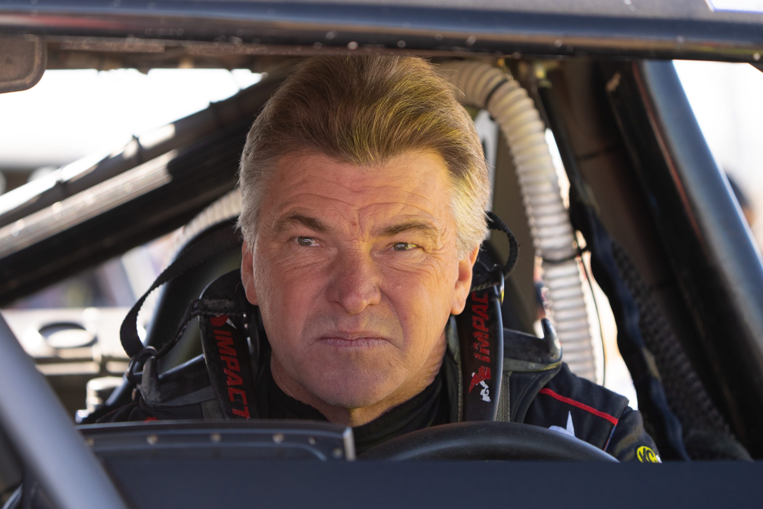 close-up photo of drag racing legend, Rob MacCachren, sitting inside his off-road trophy truck at the 2022 Mint 400 race. He is not driving nor is he wearing a helmet. The photo is from the front of the truck looking into the cab of the truck