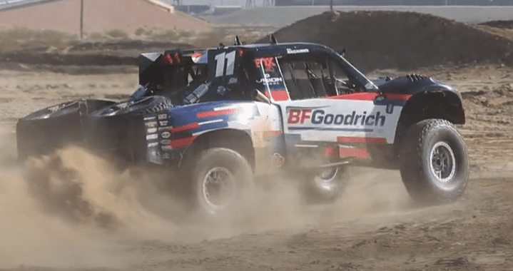 Rob MacCachren racing in the desert in his BF Goodrich Trophy Truck. Photo is a side view of his truck with a trail of dirt trailing the truck