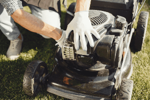 man wearing white work gloves working on lawn mower that won't start