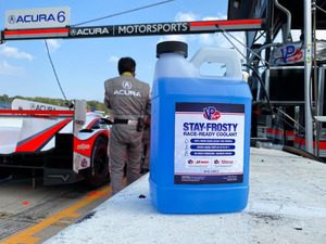 1 gallon bottle of Stay Frosty Race Ready Coolant sitting on a concrete ledge in the pits of a race track. A crew member and racecar are in the background