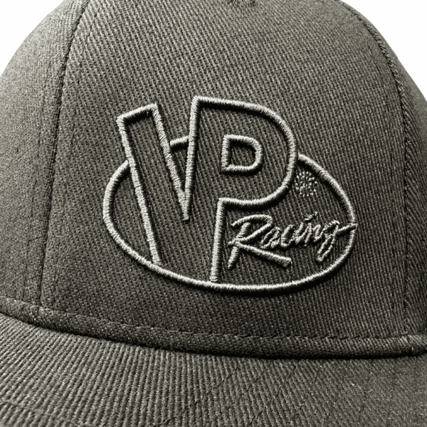 VP's flat bill hats include this Makin' Power! cap. Photo shows close-up of front of the 6-panel cap, with a greyish monochrome-type VP Racing logo embroidered on the front left panel