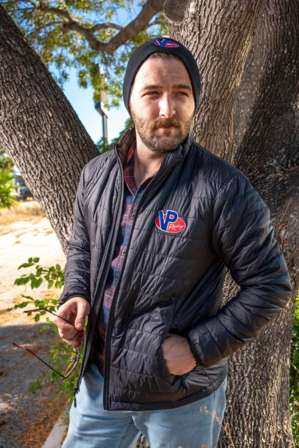 Lifestyle image of male model outside and wearing the VP Turbo Jacket. His left hand in his jacket pocket and he's holding a pair of sunglasses in his right hand